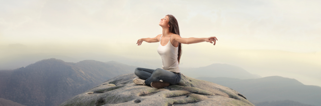 Девушка медитирует на природе, на вершине горы, раскинув руки в стороны